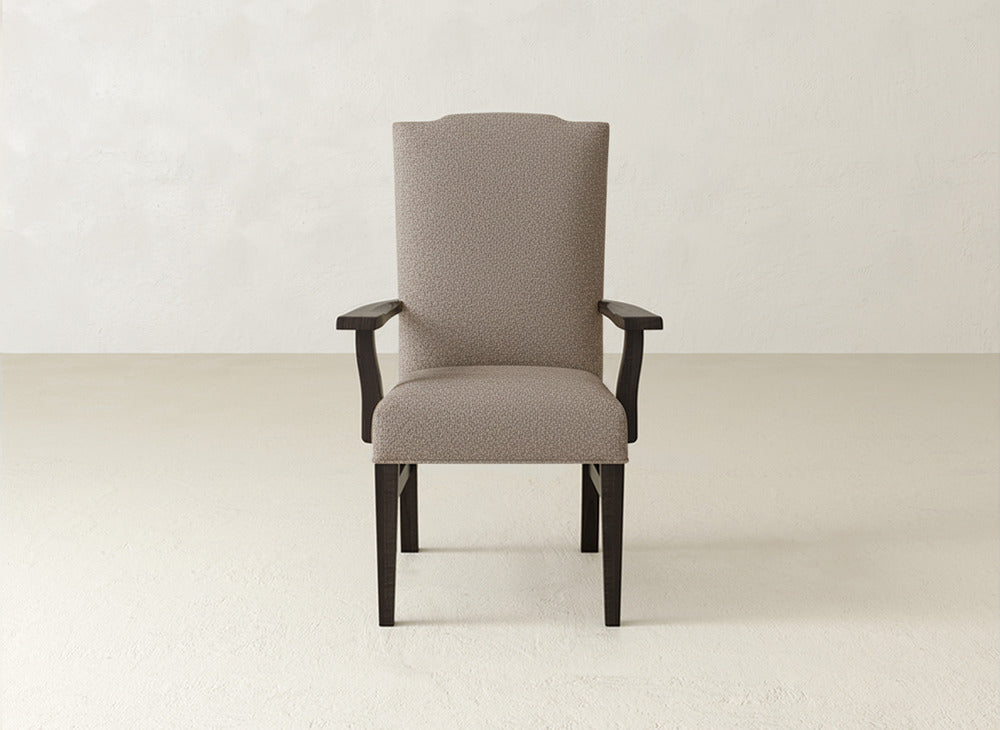 A Hadley Arm Dining Chair by James+James, with a high backrest and dark wood legs and armrests, sits elegantly in an empty room with a light floor and plain off-white wall.