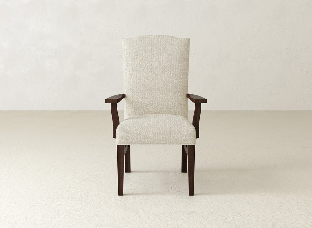 A beige Hadley Arm Dining Chair by James+James with dark wood legs and armrests is centered in an empty, light-colored room with textured walls and flooring.
