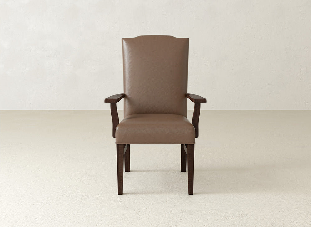 A brown James+James Hadley Arm Dining Chair with a high back and plush upholstery sits centered in an empty room with a light-colored textured wall and floor.