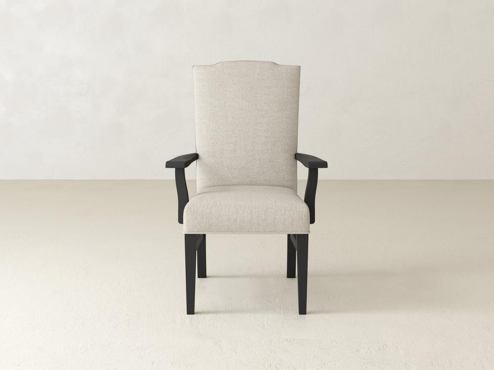 A single beige upholstered armchair with dark wooden legs and armrests, centered against a plain light-colored wall and floor background. The chair has a tall backrest with a slightly curved top.