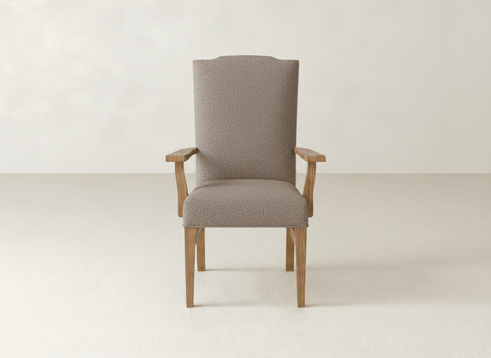 The Hadley Arm Dining Chair by James+James features a high, curved back, textured light brown upholstery, and wooden arms and legs, centered against a plain light background.
