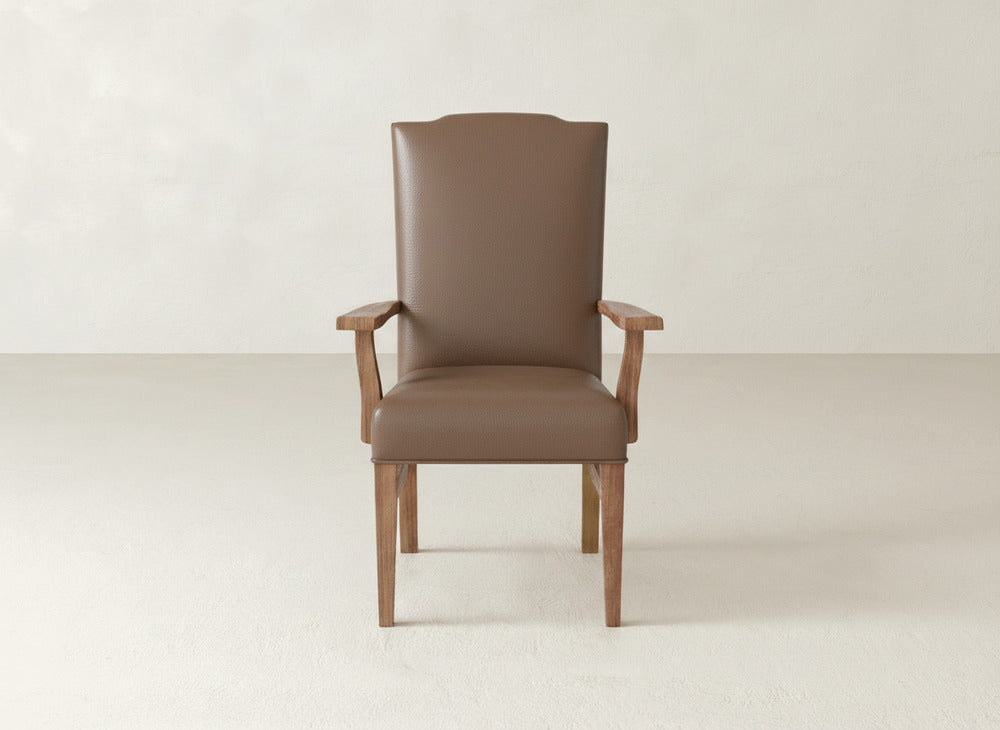 A brown Hadley Arm Dining Chair by James+James, featuring wooden arms and legs, sits centered in a light room with neutral walls and a smooth floor, offering high-back style and comfort to any space.