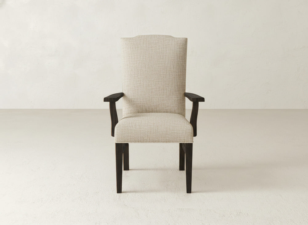 A beige James+James Hadley Arm Dining Chair with dark wooden legs and armrests is centered in a minimalist room with off-white walls and floor, offering the comfort of a high-back chair.