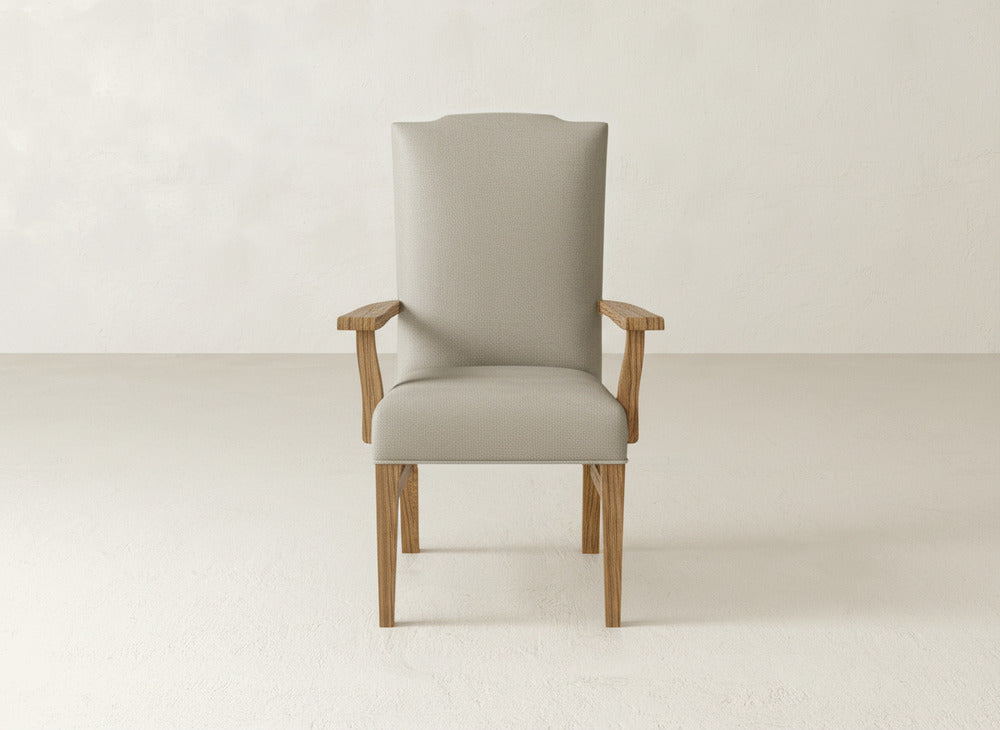 The Hadley Arm Dining Chair by James+James features light beige upholstery and wooden legs and armrests. This modern high-back chair offers comfort and contemporary style, shown here against a plain light-colored background.