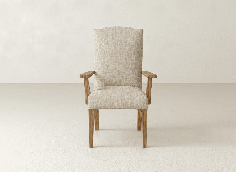 The James+James Hadley Arm Dining Chair, upholstered in beige with wooden legs and armrests, is set in a minimal, light-toned room with a plain background for stylish comfort.