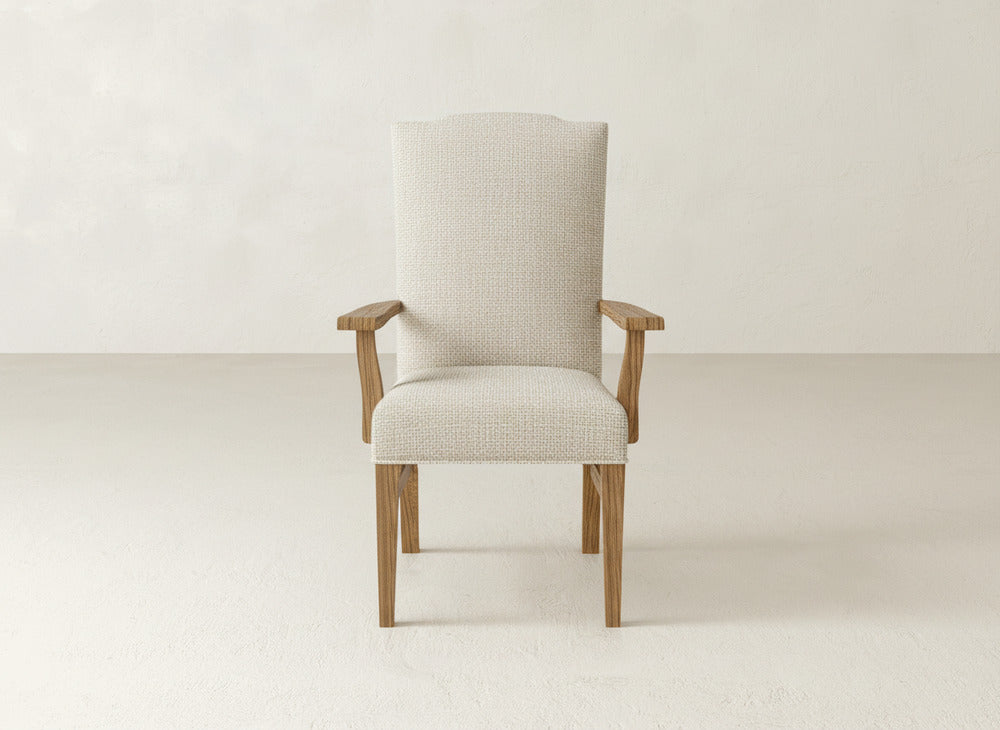 A beige Hadley Arm Dining Chair by James+James, featuring wooden legs and armrests, is centered in a minimalist room with light floors and walls, offering an ideal mix of comfort and style.