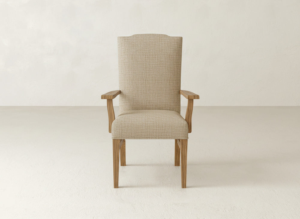 The James+James Hadley Arm Dining Chair in beige upholstery, featuring light wood arms and legs, is centered against a minimalist light wall and floor.