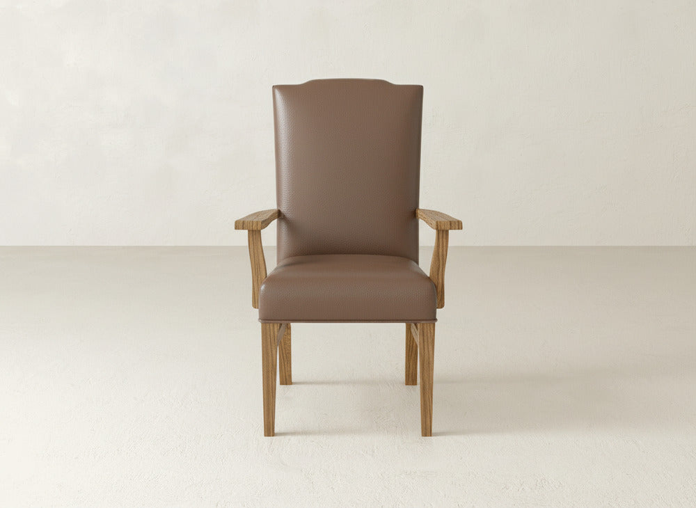 The Hadley Arm Dining Chair by James+James, featuring brown upholstery, wooden legs, and armrests, is set against a plain light wall and floor background.