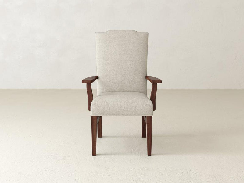 The Hadley Arm Chair Set of Four - Tuscany & Cream by James+James, with its heirloom-quality design, features beige upholstery and wooden armrests and legs. It enhances the minimalist, light-colored room with its clean aesthetic.