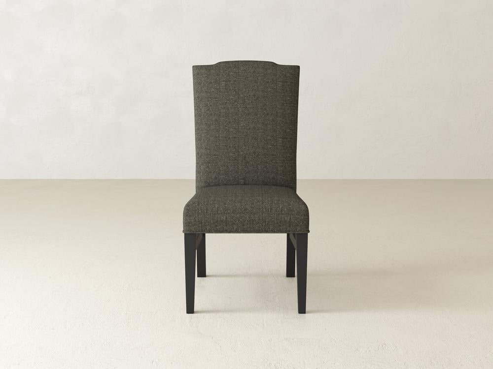 A single, upholstered chair with a tall backrest and dark wooden legs, placed against a plain, light-colored wall on a light floor.
