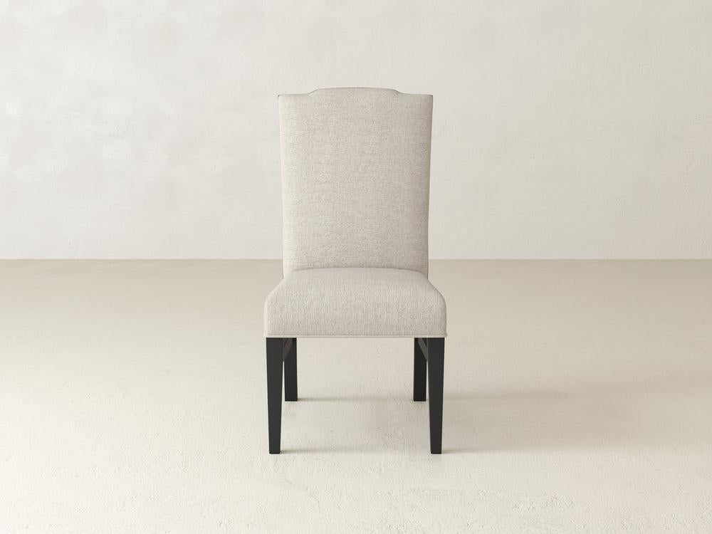 A light gray upholstered dining chair with a high backrest and black wooden legs, positioned centrally against a plain, light-colored wall background.