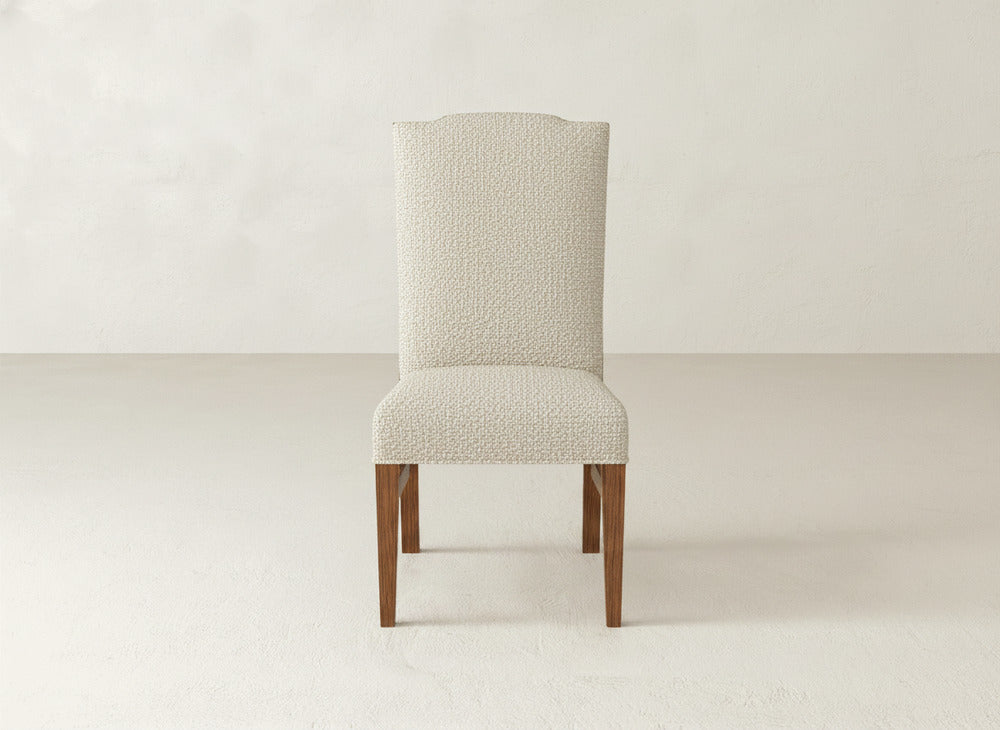 The Hadley Side Dining Chair by James+James features a tall, high back, light textured upholstery, and wooden legs, beautifully set against a plain, light-colored background.