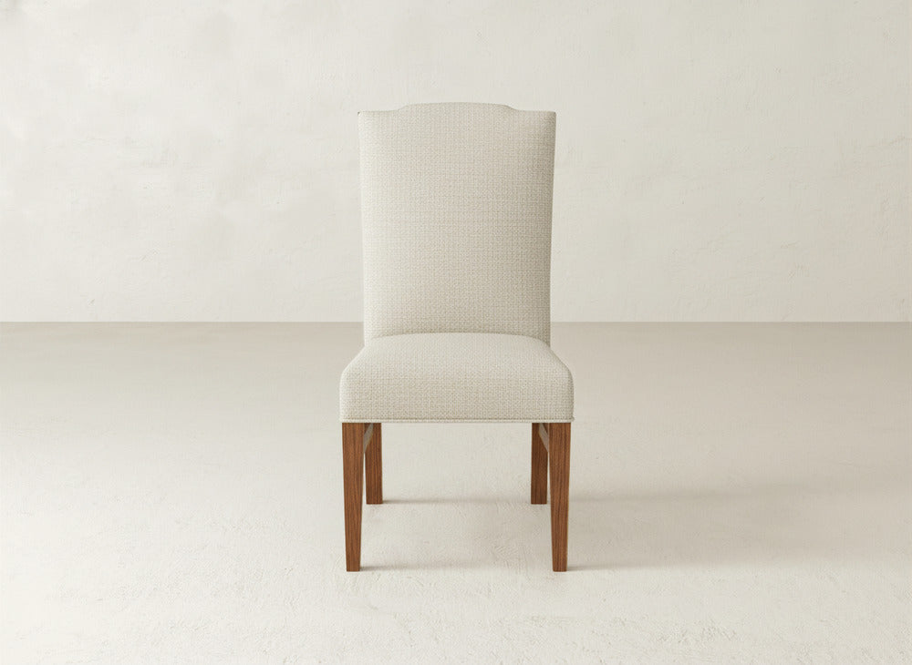 A straight-on view of the James+James Hadley Side Dining Chair, featuring beige upholstery, a tall backrest, and wooden legs against a light background. This elegant chair brings sophistication to any dining space.
