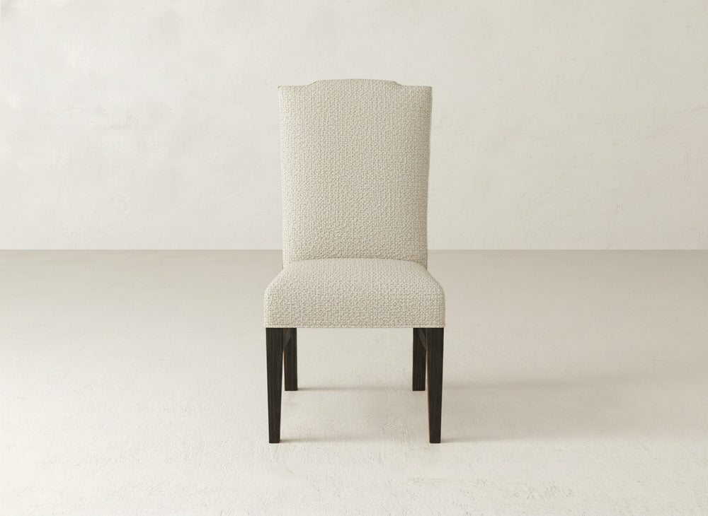The Hadley Side Dining Chair by James+James features a modern high back, light textured upholstery, and dark wooden legs, shown against a plain, light-colored background.