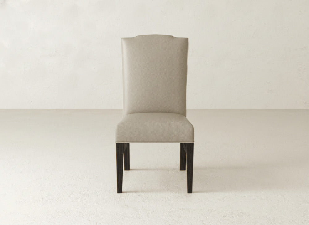 The Hadley Side Dining Chair by James+James features a tall, light gray upholstered backrest and seat, complemented by dark wooden legs, set against a plain, light-colored background.