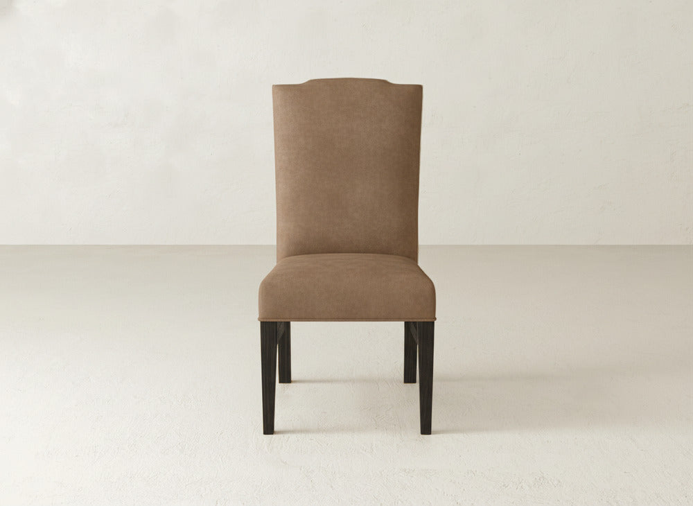 The Hadley Side Dining Chair by James+James features brown upholstery, a high back, and dark wooden legs, positioned centrally against a simple, light background.