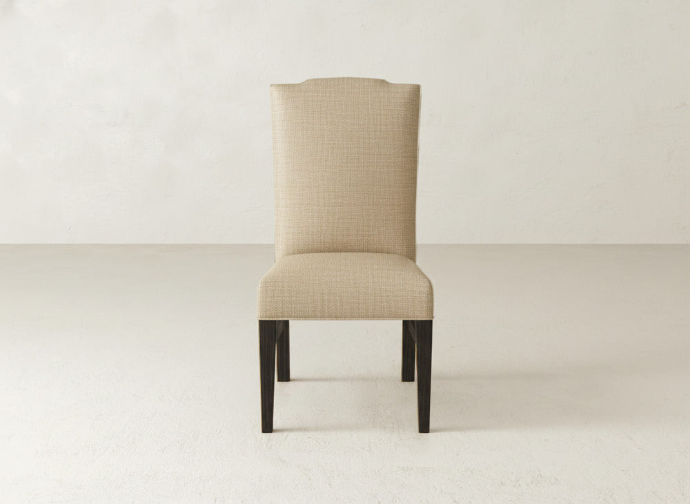 The Hadley Side Dining Chair by James+James features beige upholstery, a tall, slightly curved back, and dark wood legs, shown here on a light floor with an off-white wall background.