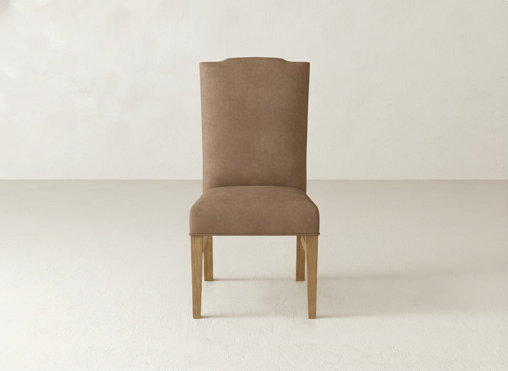 The James+James Hadley Side Dining Chair, featuring brown upholstery and wooden legs, is centered in a minimal, light-toned room with smooth, plain walls and flooring.