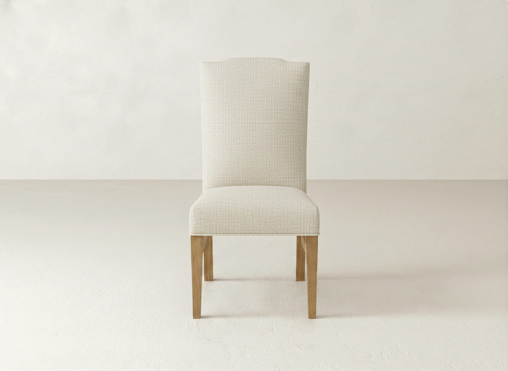 The Hadley Side Dining Chair by James+James features a modern upholstered light beige seat and backrest, wooden legs, and subtle tack detailing, shown against a plain off-white background.