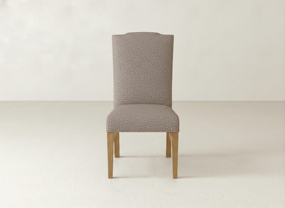 The James+James Hadley Side Dining Chair features light beige patterned fabric, subtle tack detailing, and four light wood legs, showcased in a minimalist room with pale floors and walls.