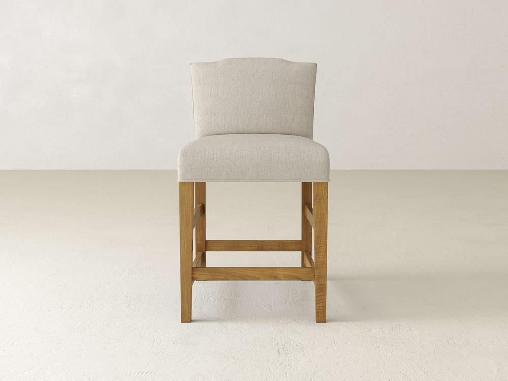 The James & James Hadley Upholstered Stool features a beige finish and wooden legs, elegantly resting on a light floor. Its high back harmonizes with the minimalist off-white wall, crafting a clean, modern ambiance.
