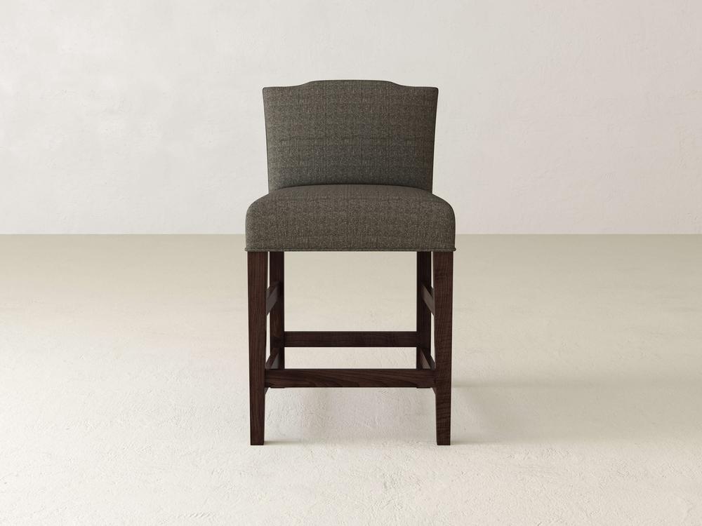 The Hadley Upholstered Stool by James & James showcases elegant gray upholstery against a light backdrop. Its modern design features dark wooden legs and a slightly curved high backrest for enhanced comfort.