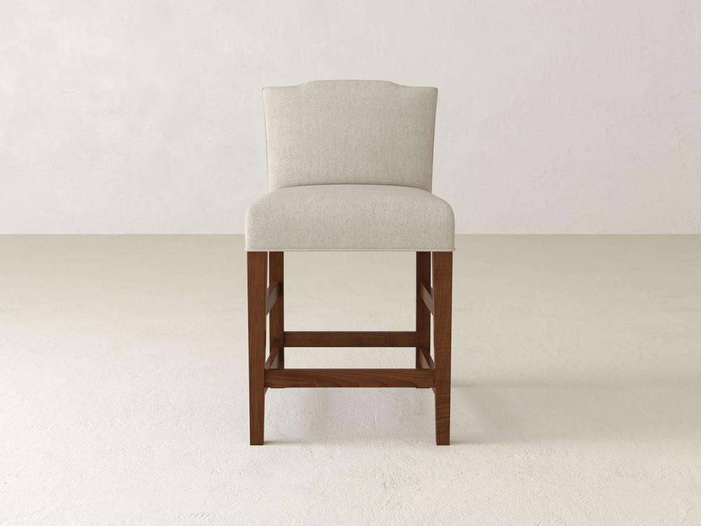 The Hadley Upholstered Stool by James & James exudes simple elegance, featuring a beige upholstered seat, wooden frame, square legs, and a slightly curved backrest. Ideal against an off-white wall or light floor, it enhances dining spaces with its refined design.