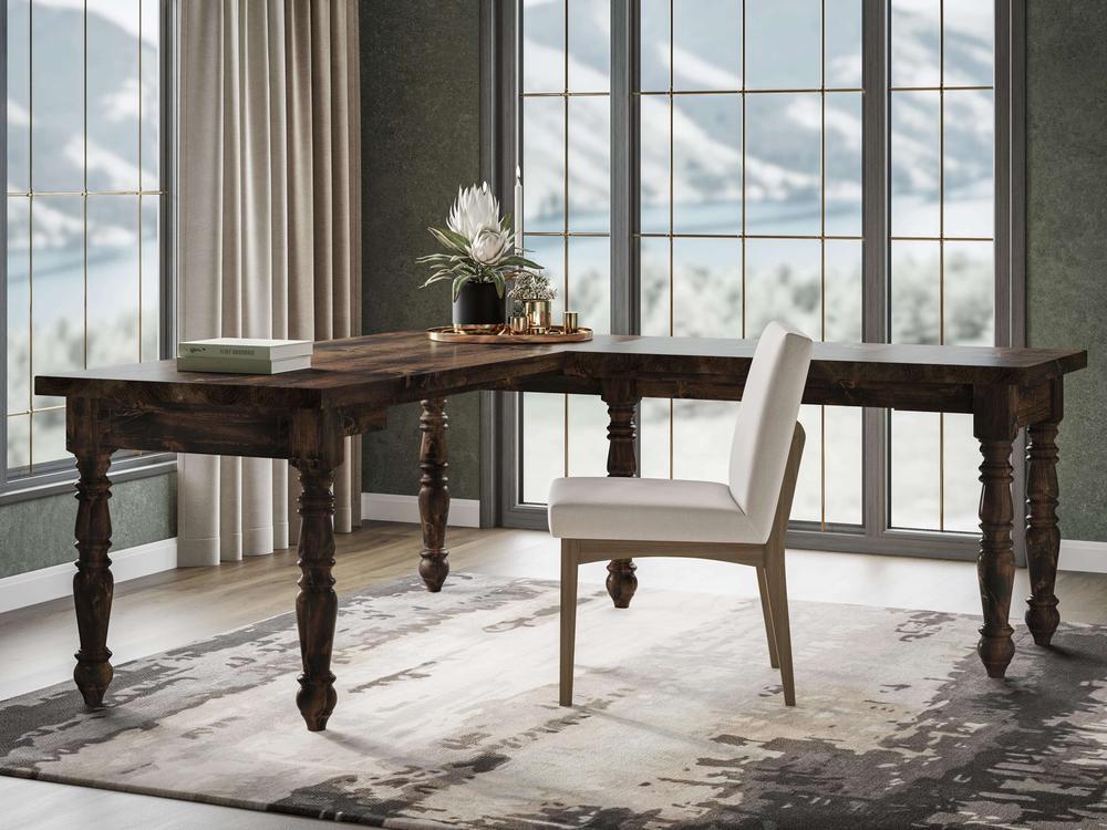 A stylish home office features the Turned Leg Corner Desk - Tobacco from James+James, showcasing its elegant turned legs. A white upholstered chair is placed near the desk. The room has large windows with a snowy mountain view, and the floor is covered with a neutral-toned rug. A plant and books adorn the desk.