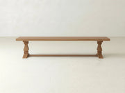 The Heirloom Bench - Oat on Oak by James+James features a rectangular seat, turned legs, and a support bar, shown against a light-colored wall and floor.
