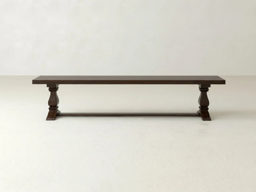 The James+James Heirloom Bench - Sable on Oak, featuring carved legs and a simple rectangular seat, is set against a plain, light-colored wall and floor.