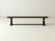 The James+James Heirloom Bench - Sable on Oak, featuring carved legs and a simple rectangular seat, is set against a plain, light-colored wall and floor.