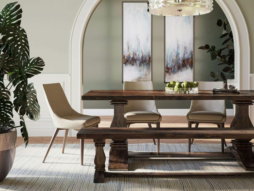A modern dining room with a wooden table, four beige chairs, the James+James Heirloom Bench - Tobacco on Alder, a bowl of green apples, abstract wall art, a potted plant, and a large archway leading to another room.