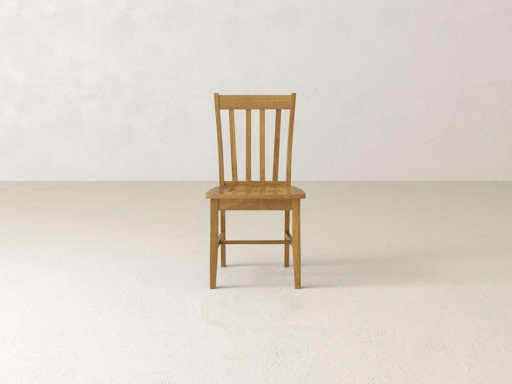 Wooden chair with a simple design and vertical slats on the backrest, placed in the center of an empty room with a plain beige floor and wall.