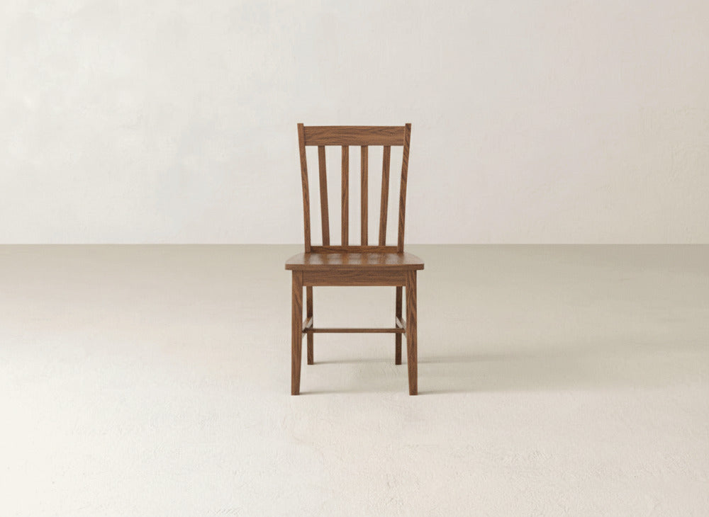 A single James+James Henry Dining Chair, featuring a classic slat-back design, is centered in an empty, light-colored room with a plain wall and floor.