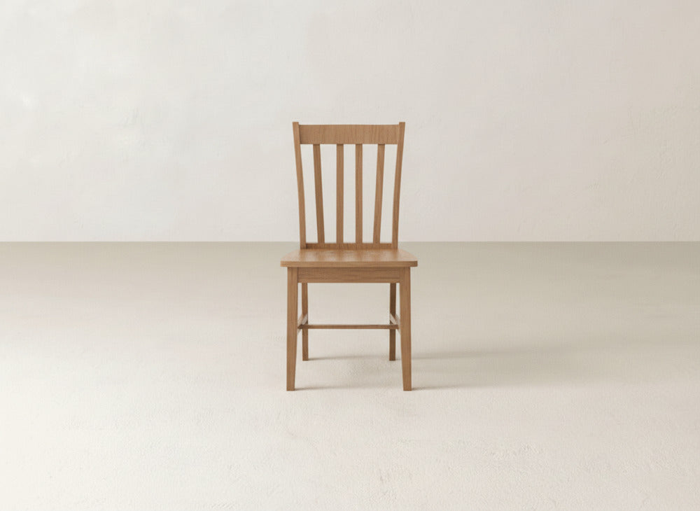 The Henry Dining Chair by James+James, featuring a classic slat-back design, stands in a bright, minimalist room with pale walls and flooring, embodying refined dining style.