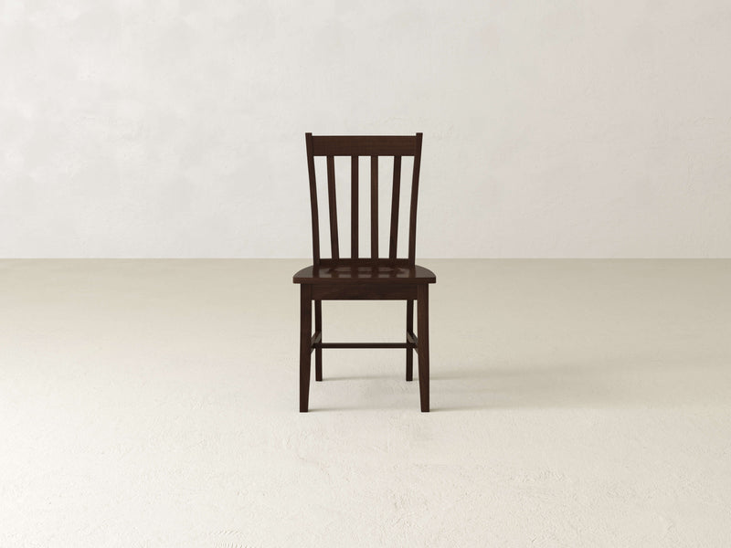 The Henry Dining Chair - Tobacco by James+James features a wooden design with a high backrest adorned with vertical slats. The chair boasts a dark wood finish and four straight legs, showcasing simple and sturdy construction. Its flat seat complements the classic and minimalist design, as shown from an angled rear view.