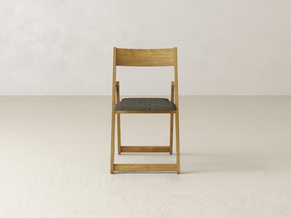 A wooden folding chair with a dark cushioned seat is placed against a plain, light-colored background. The chair is facing the camera directly, highlighting its simple and elegant design.