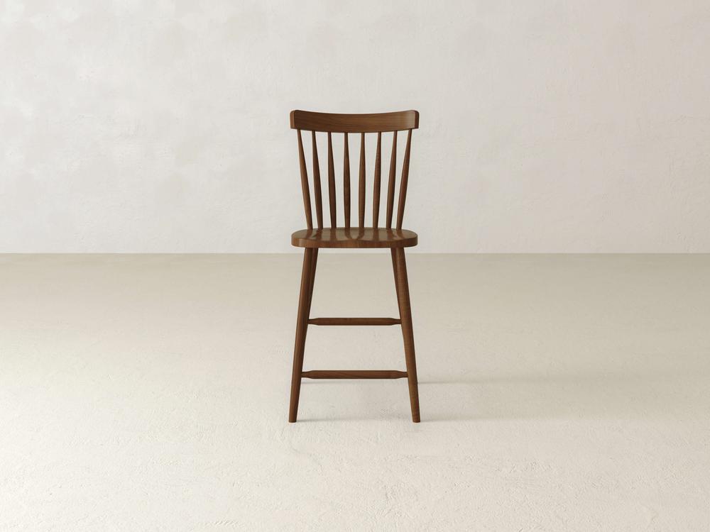 The Rustic Windsor Swivel Stool by James & James showcases a sleek, minimalist design with an elegant spindle backrest. Made of durable maple hardwood, it stands against a plain white background and features four legs connected by horizontal bars.