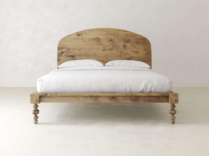 The Olivia Arch Bed - Harvest Wheat by James+James features an arched headboard and turned legs, complemented by white bedding and two pillows, set against a light, neutral background for a minimalist rustic design.