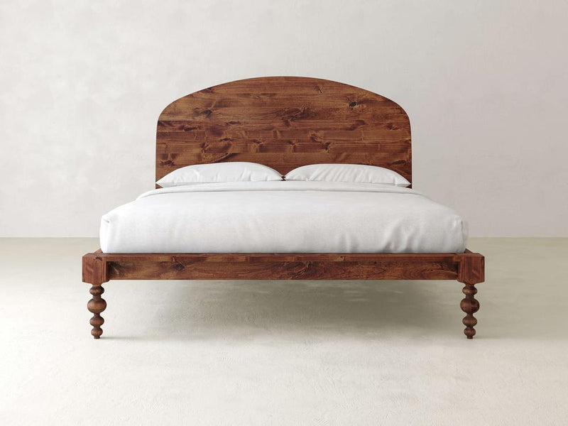 The Olivia Arch Bed - Tuscany from James+James features a curved headboard and turned legs in polished wood, complemented by a white mattress and two pillows. It rests against a plain, light-colored wall.