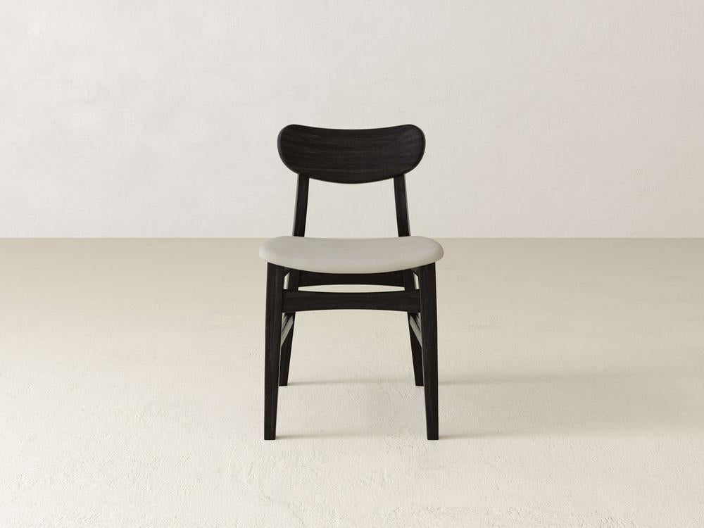 A modern chair with a black wooden frame and a white cushioned seat is centered in a minimalist room. The background is a plain, light-colored wall and floor.