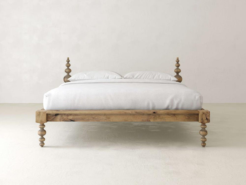 The Olivia Platform Bed in Harvest Wheat by James+James features a wooden frame with intricate spindle legs and posts, supporting a neatly made white bed with two pillows against a plain white background.