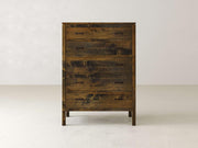 The James & James Jensen Tall Chest, made from solid maple hardwood, features a rustic yet slightly weathered finish. Its five drawers have simple metal handles that complement contemporary designs against a plain, light-colored backdrop.