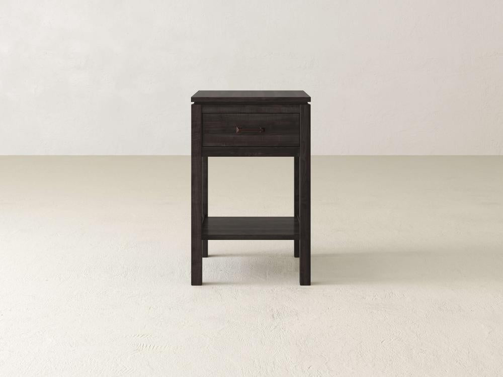 The Jensen 1 Drawer Nightstand by James & James, made from solid maple hardwood, showcases modern simplicity with its minimalist design. This dark wood side table features clean lines, a single drawer, and a lower shelf set against a plain white background.