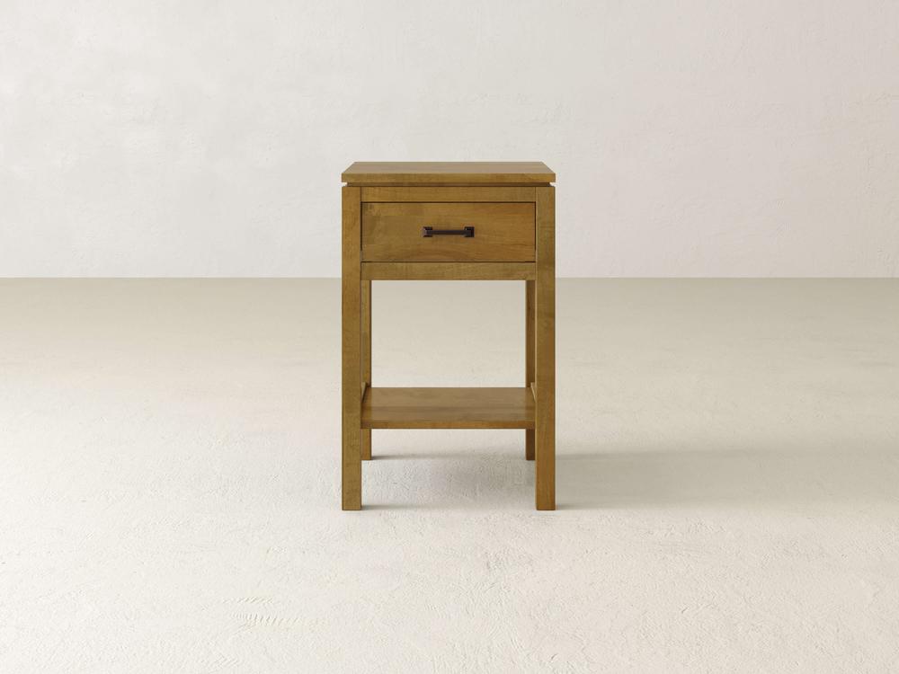 The Jensen 1 Drawer Nightstand by James & James highlights modern simplicity with its solid maple hardwood construction, light brown finish, sleek black-handled drawer, and lower shelf, all set against a plain, light-colored background.