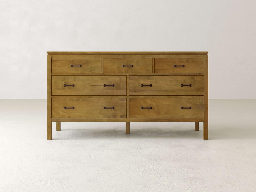 The James & James Jensen 7 Drawer Dresser, crafted in solid maple with a natural finish, features three top small drawers and four large ones below, each with dark handles. It offers a contemporary touch against light walls and floors.