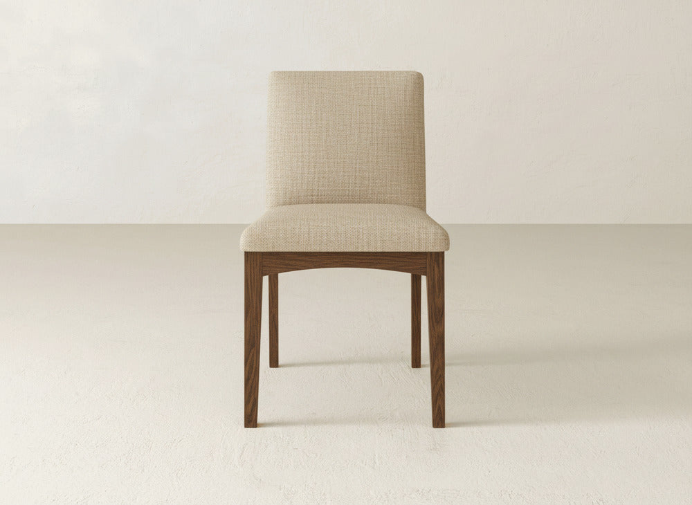 The Klein Dining Chair by James & James features maple wooden legs and a light beige cushioned seat and backrest, set on a plain, light-colored floor with a neutral wall background.
