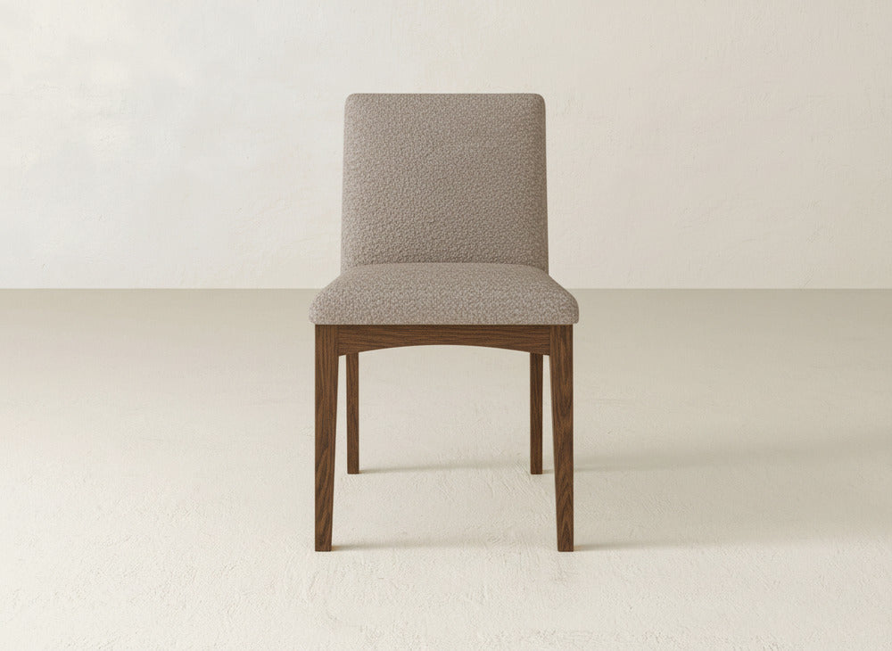 The Klein Dining Chair by James & James features a modern upholstered design with a light beige seat and back, sturdy maple legs, and is shown on a light floor with a plain, light backdrop.