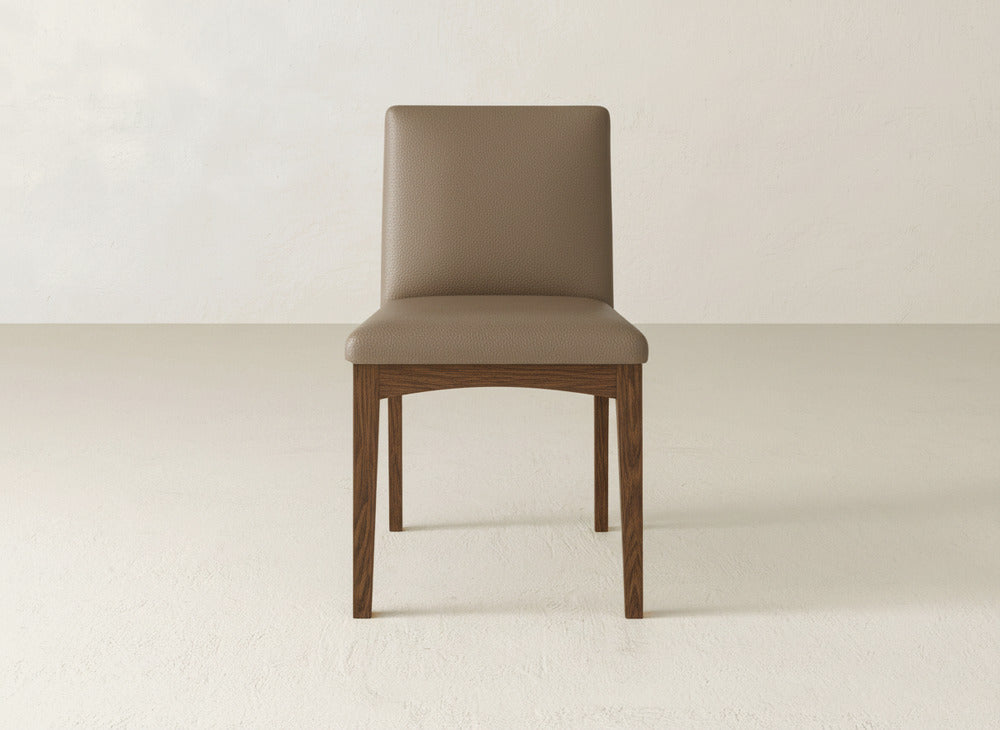 The Klein Dining Chair by James & James features a modern upholstered design with a brown cushioned seat and backrest, maple wooden legs, and is shown on a light floor against an off-white wall.