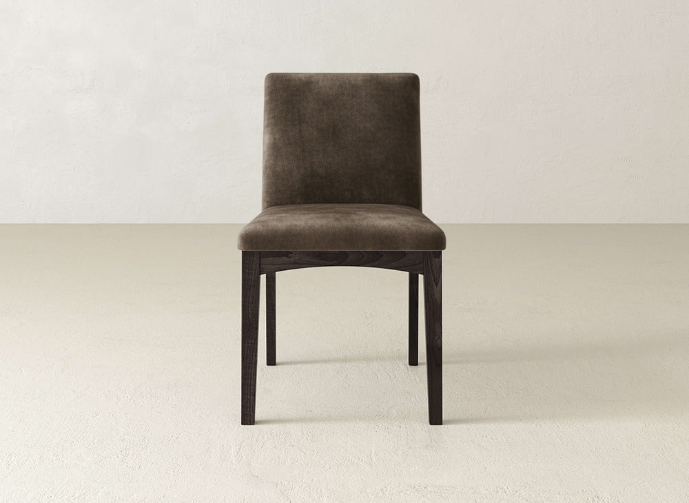 A single brown Klein Dining Chair by James & James, featuring a straight back and maple wooden legs, is placed on a light-colored floor against an off-white wall.